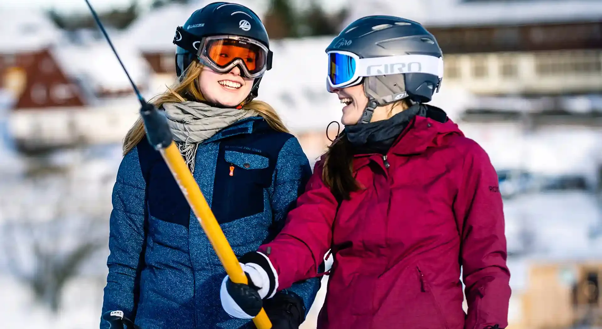 Zwei Skifahrerinnen mit Helmen und Skibrillen nutzen den Skilift Altenberg am Erlebnisberg Altenberg und lachen in winterlicher Umgebung.